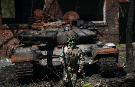 A Ukrainian soldier standing next to a destroyed Russian tank.
