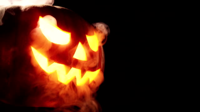 Scary carved halloween pumpkin in hot burning hell fire flames. The big helloween pumpkin has a mad face with glowing eyes and also a smoke in its mouth and teeth.