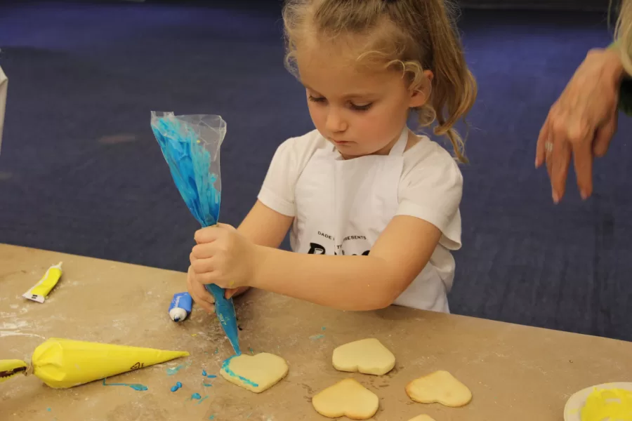 A Ukrainian refugee little girl decorates her cookies in her favorite color, blue.