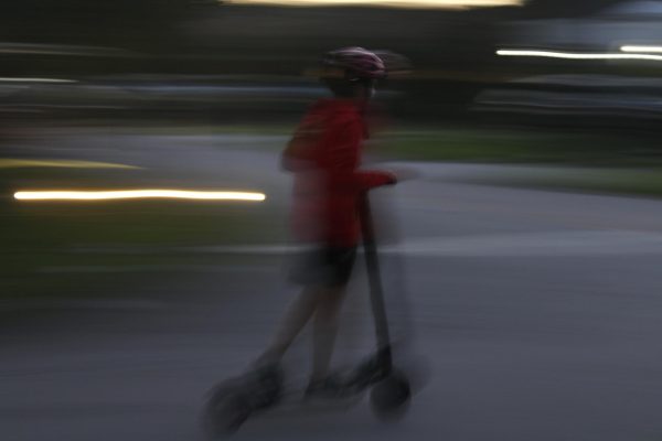 A rider on an electric scooter zooms by so quickly it is difficult to capture a still shot.