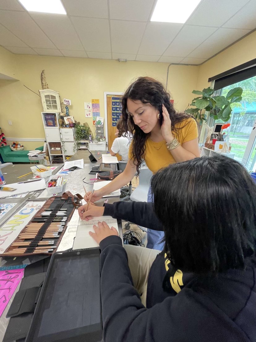 Art teacher Ms.Camille Wildenburg works on artwork with a student.