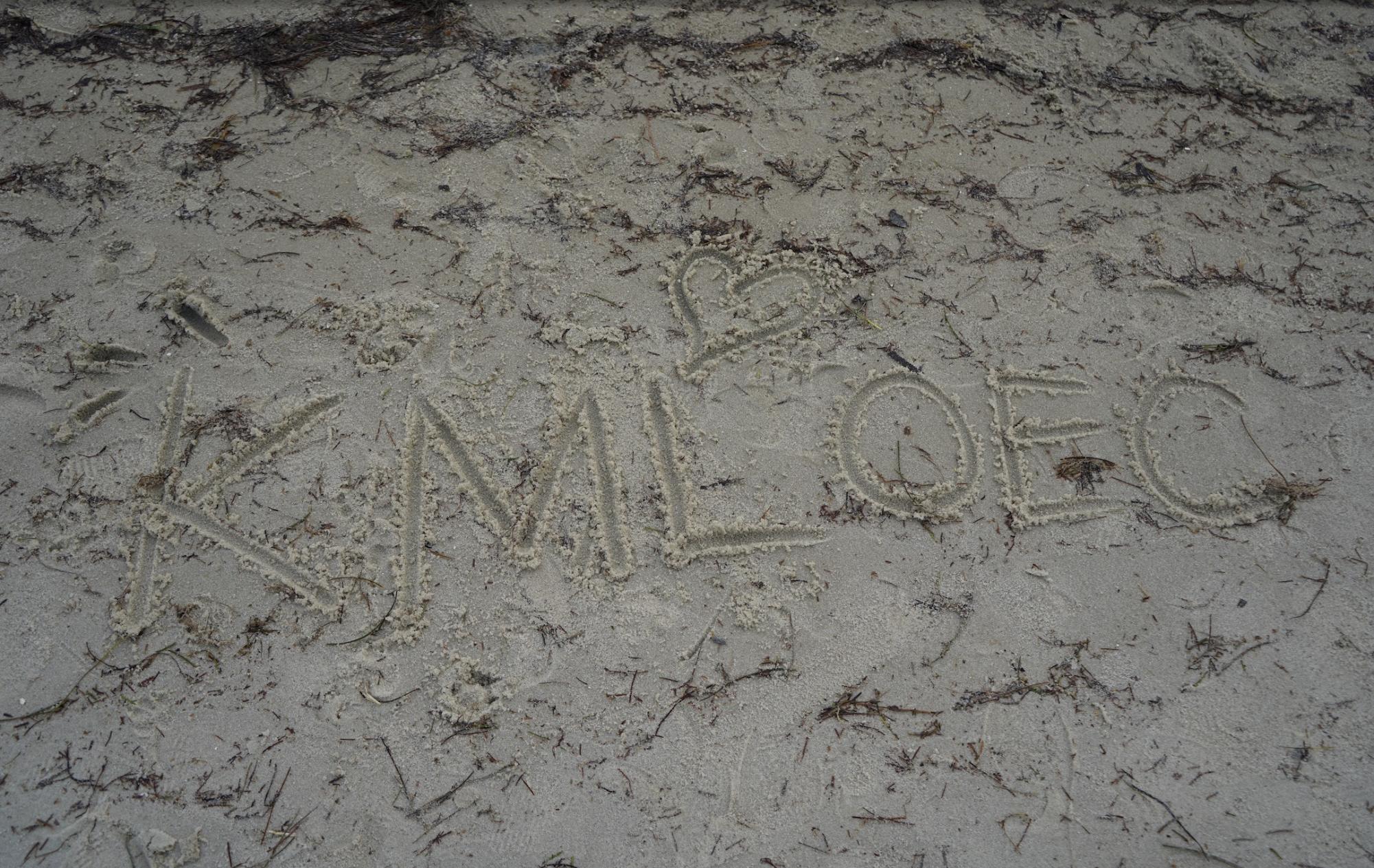 The initials of the non-profit organization, KMLOEC, carved in the sand.