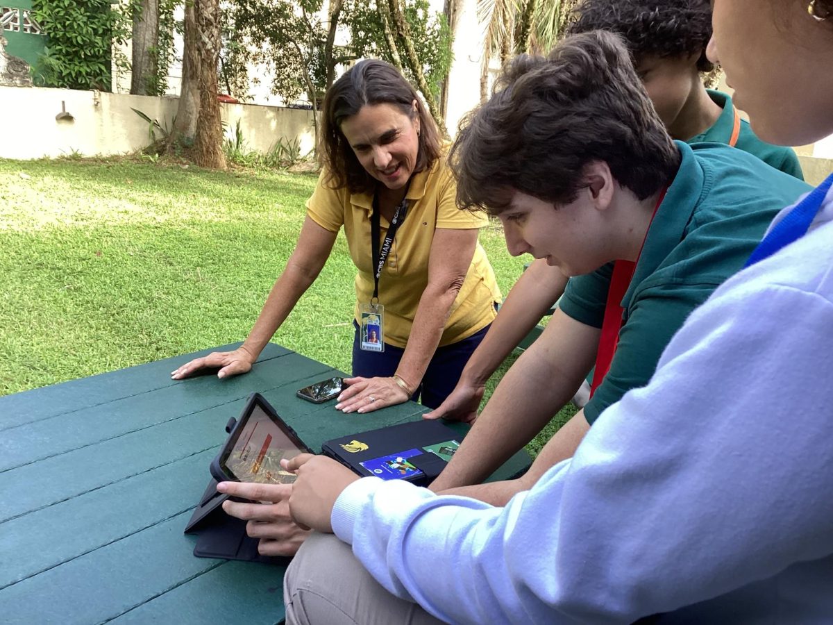 Ms. Cristina Ramirez, journalism adviser, watches senior Miguel Suarez Cabal take the iPad challenge quiz to find out if he should be burned at the stake.