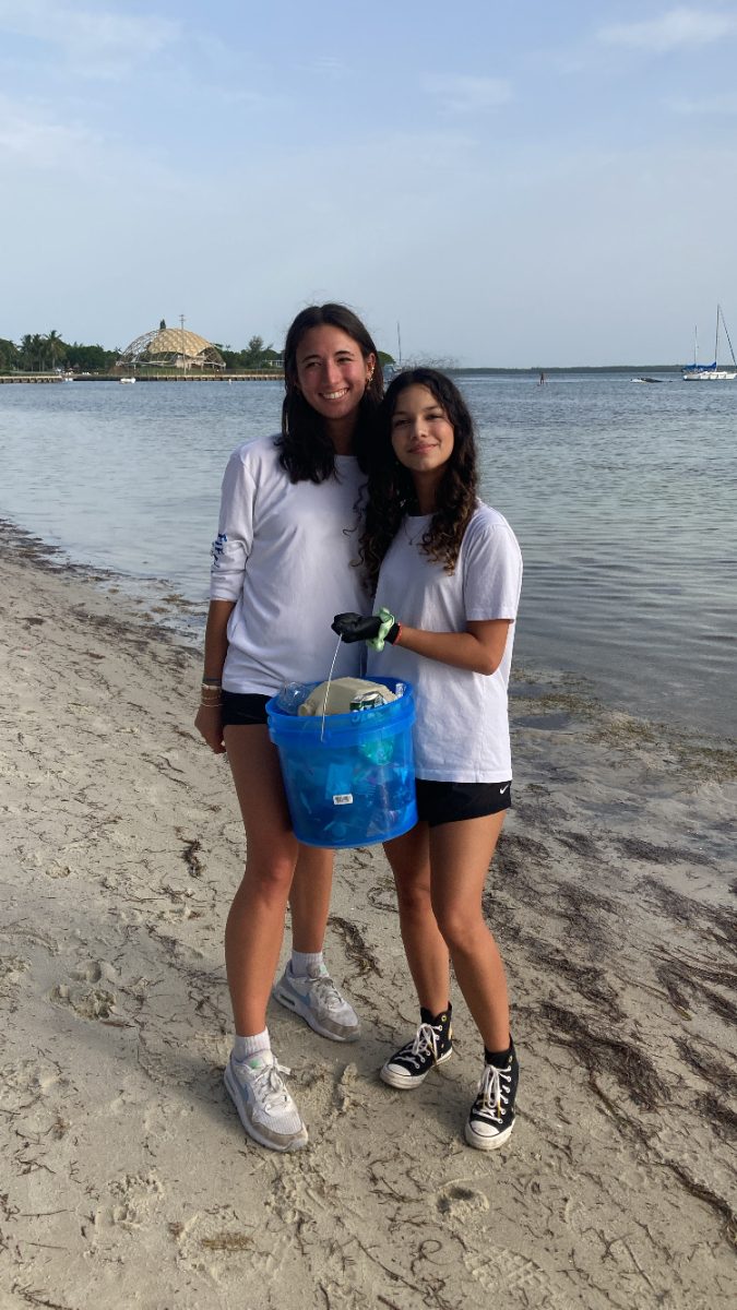 Standing by the shoreline, KMLOEC volunteers hold a bucket full of collected plastic waste. The group’s cleanups prevent pollution from entering Miami’s waterways, protecting marine ecosystems from harmful debris.