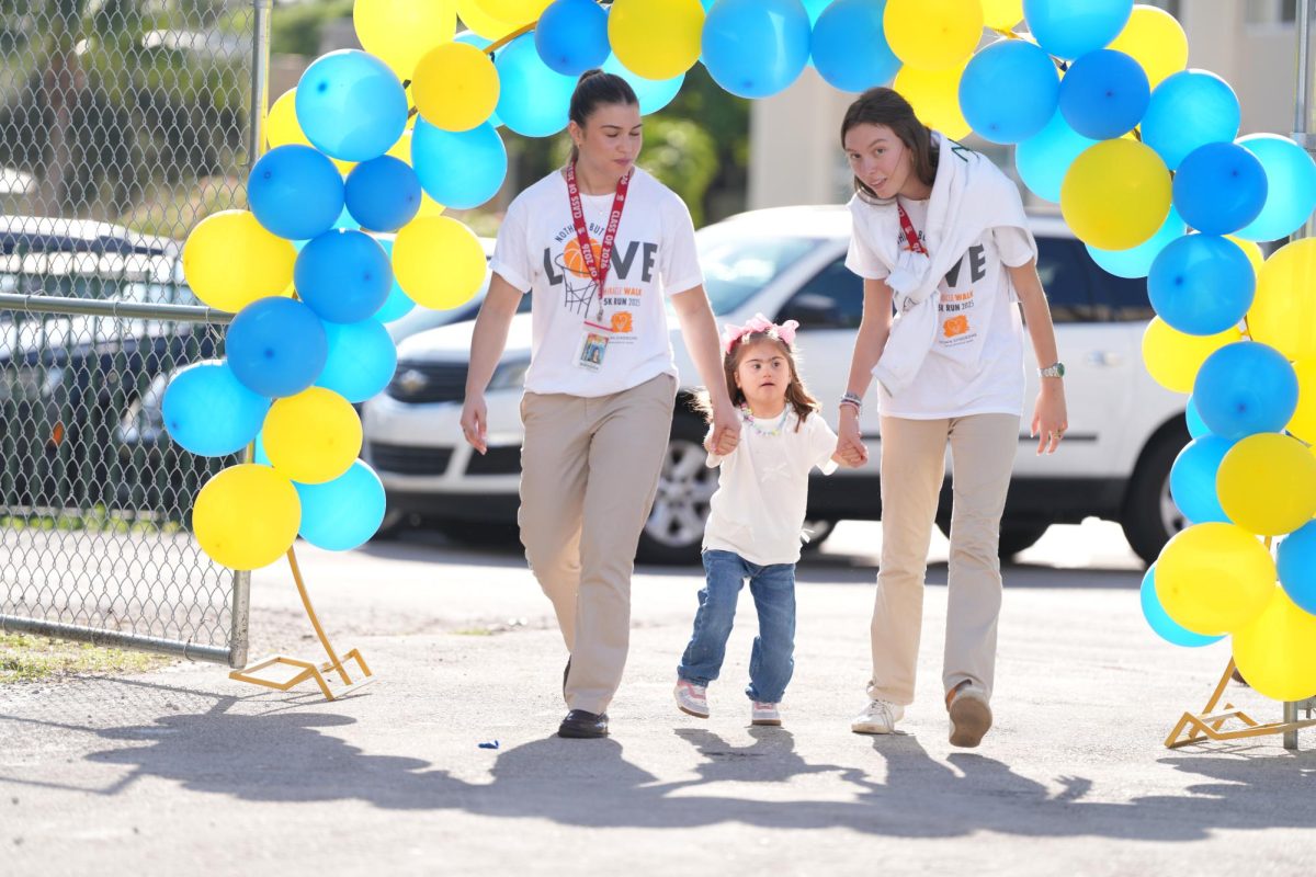 Volunteers and a visitor from the Learning Experience walk under the welcoming balloon arch on the track at ILS, site of the annual Miracle Walk.