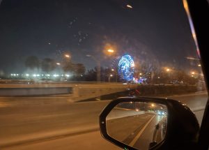The Ferris wheel at Christmas Wonderland glows beside the highway at night.