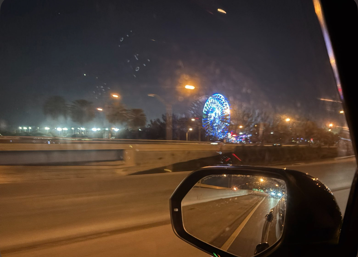 The Ferris wheel at Christmas Wonderland glows beside the highway at night.