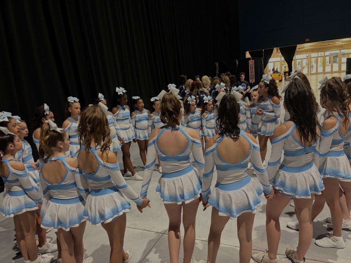 Members of Idol Gems, gather in a tight huddle to pray together before walking onto the mat. This moment shows the team relying on one another for support and focus before competing at the Daytona cheer championships.