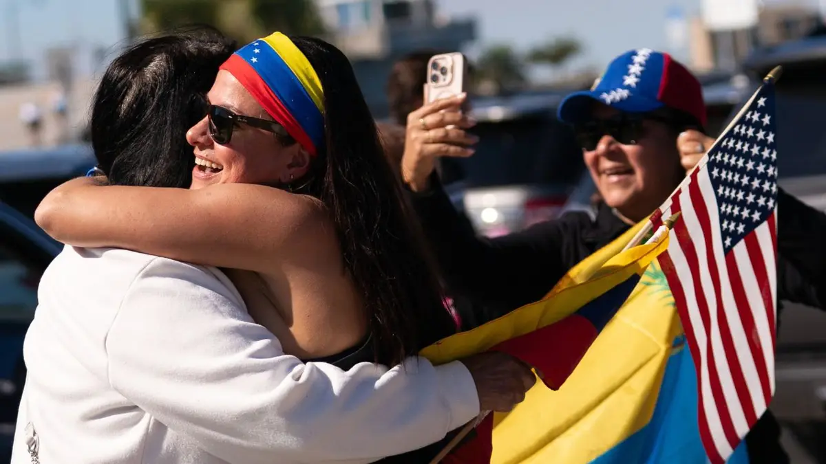 A Venezuelan woman seen hugging another person in celebration drapped in Venezuelan and American flags.