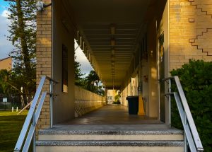 An empty hallway during class time. The lines of the walkway lead the eye toward the light, representing the quietest moments of the school day.
