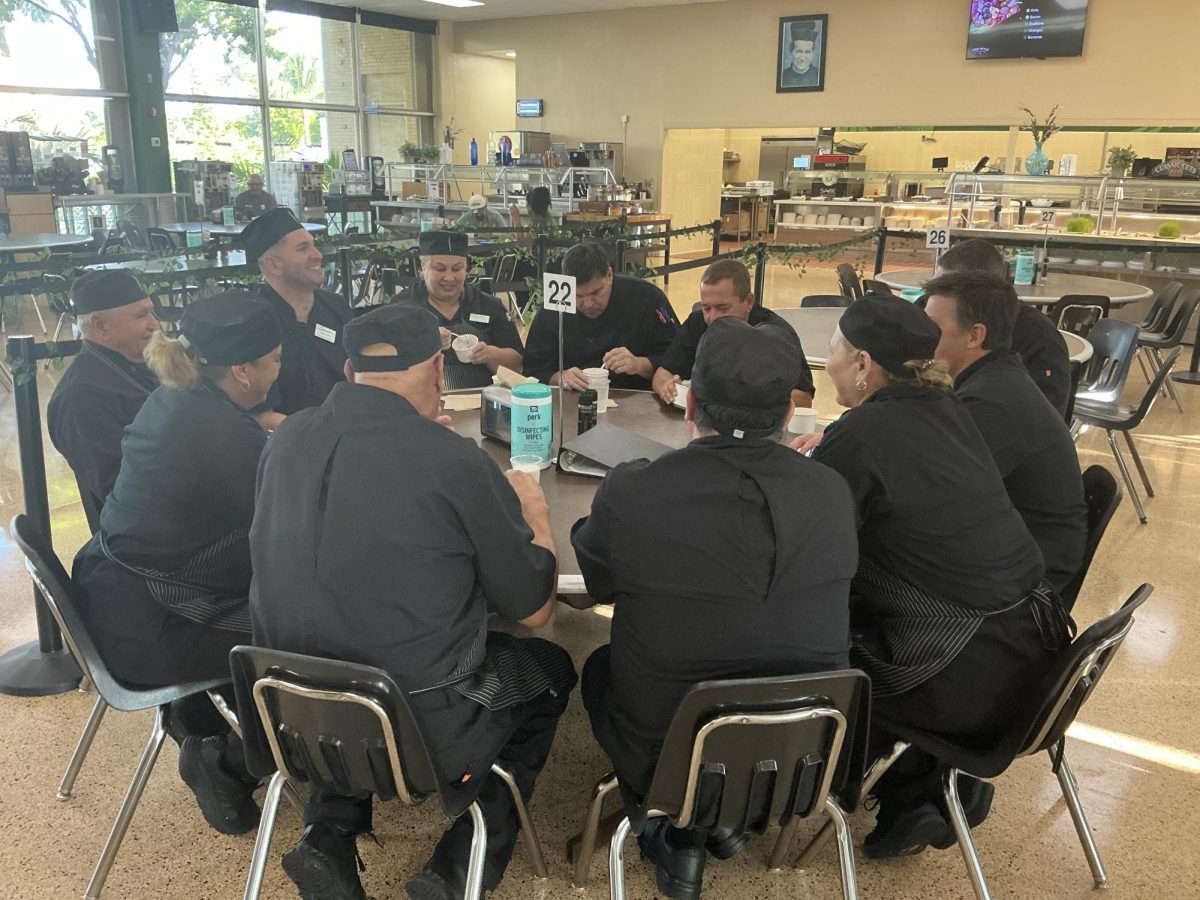 Cook Roberto Martinez shares laughs with his fellow culinary team members during a morning meal at ILS. Swapping stories and chatting in Spanish over breakfast, the staff took a brief break together in the cafeteria before starting their daily prep work.